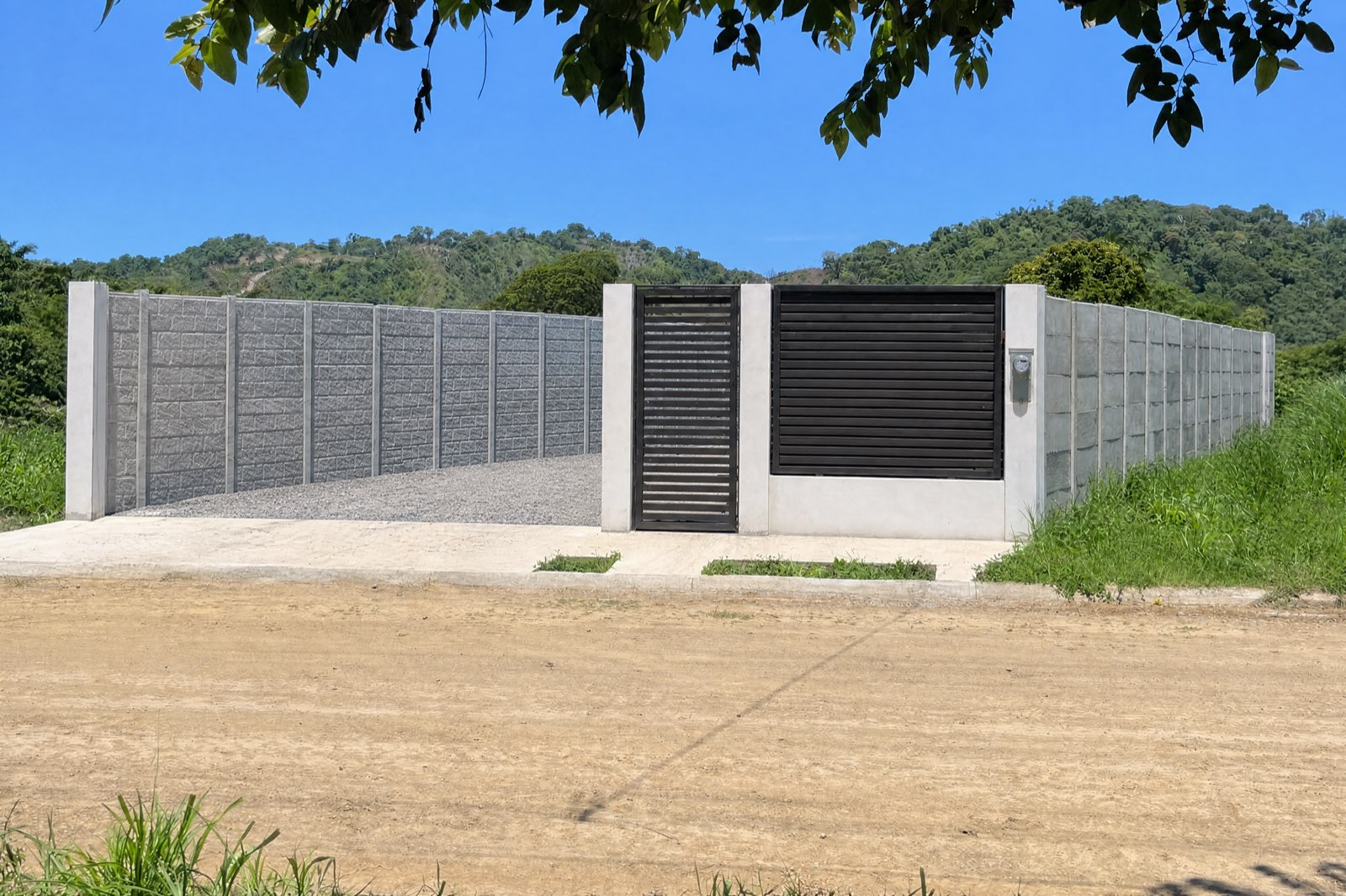 Daruma Jacó entrance — gate and wall with the Quebrada Bonita hills behind